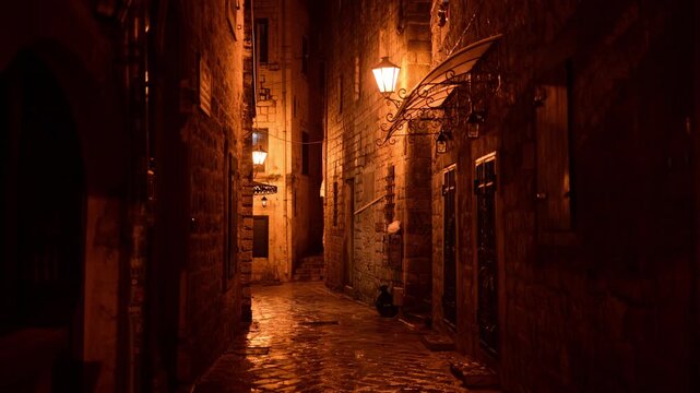 Narrow cobblestone alleyway illuminated by vintage street lamps creating a mysterious atmosphere. Kotor Old Town, Montenegro