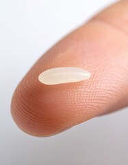 Close up Macro of a Single Grain of White Rice Resting on a Human Finger Pad Against a Softly Blurred White Background