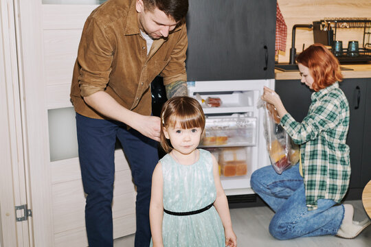 A father fixes his daughter's hair in the kitchen