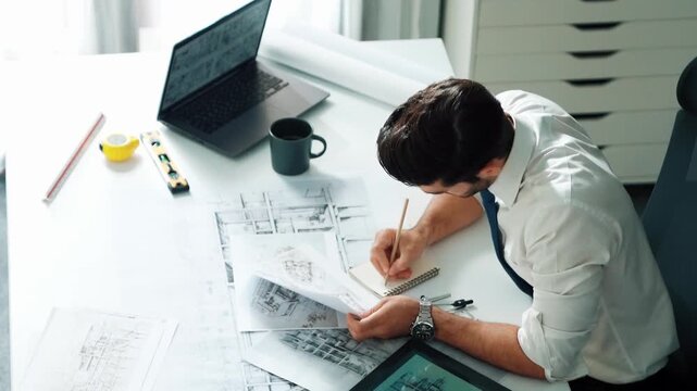 Architect engineer using laptop planning house design at office while sitting at meeting table with blueprint and equipment scatter around.Skilled civil engineer working at blueprint. Alimentation.