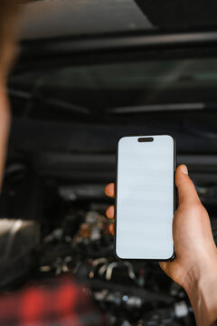 A man uses a mobile phone with white screen in a car repair shop