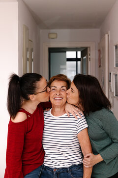 Joyful mother receiving kisses from her adult daughters