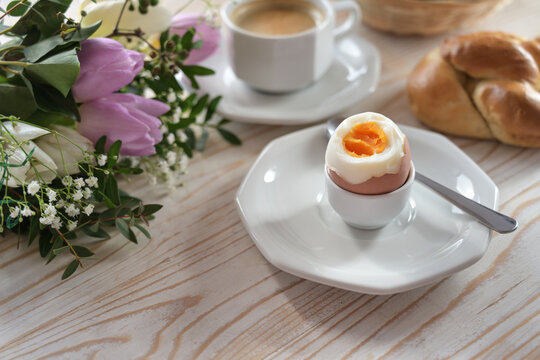 Boiled egg with soft yolk on an wooden breakfast table with buns, coffee and flowers, easter or mothers day, copy space, selected focus