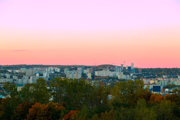 Fototapeta premium Panoramic cityscape at sunset with pastel sky and lush green trees in the foreground