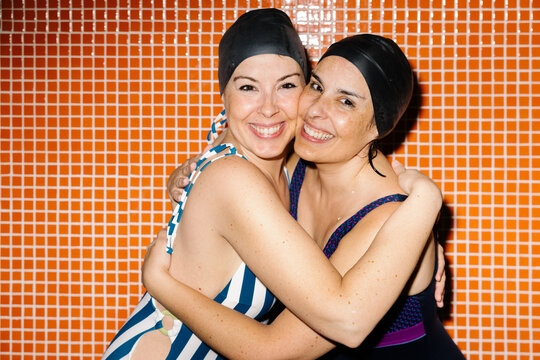 Two women in swimsuits smiling and hugging at the poolside
