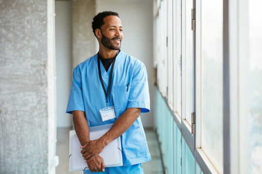 Cheerful male doctor in uniform standing near window
