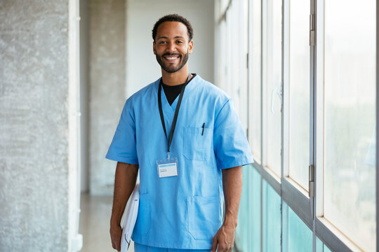 Cheerful male doctor in uniform standing near window