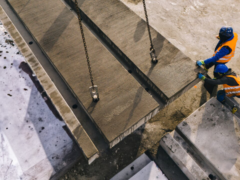 Installation of large prefabricated concrete slabs at an active construction site. Workers guiding heavy precast elements during an industrial assembly process.
