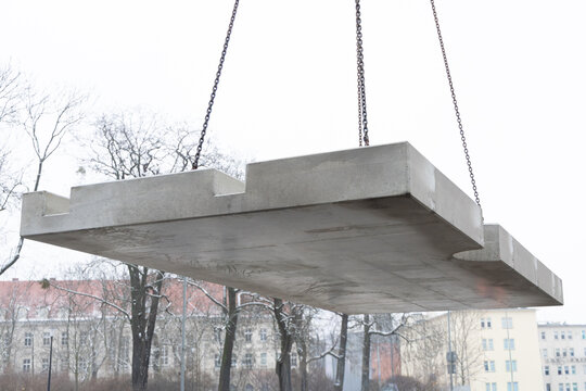 Large prefabricated concrete slab lifted by crane during installation process. Heavy precast element suspended in air at an urban construction site.