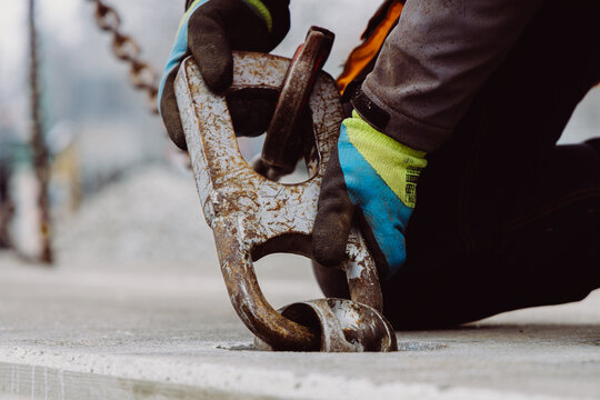 Close-up of a worker attaching a heavy steel hook to a prefabricated concrete slab. Industrial lifting equipment used during a professional construction process.