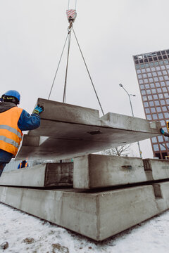 Workers installing a large prefabricated concrete slab using a crane at an urban construction site. Teamwork and heavy machinery ensure precise placement of precast elements.