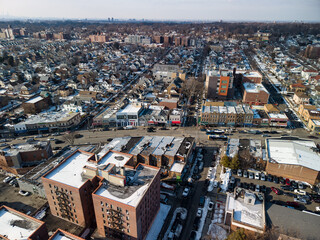 Naklejka premium Aerial view showcasing a typical hollis, queens, new york neighborhood with residential homes, commercial buildings, and streets covered in light snow during winter