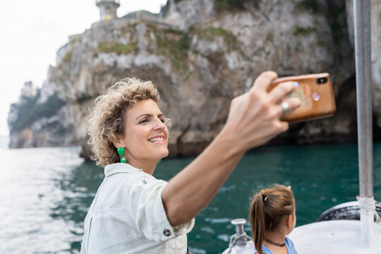 Tourist taking selfie on boat trip with cliff and sea in background