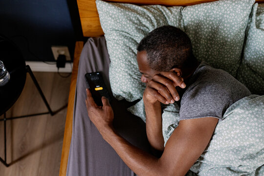 Top view of adult black man turning off alarm on smartphone in bed
