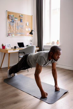 Adult black man with tattoos doing push ups on fists on fitness mat