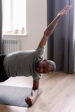Side view of adult black man doing side plank exercise on fitness mat