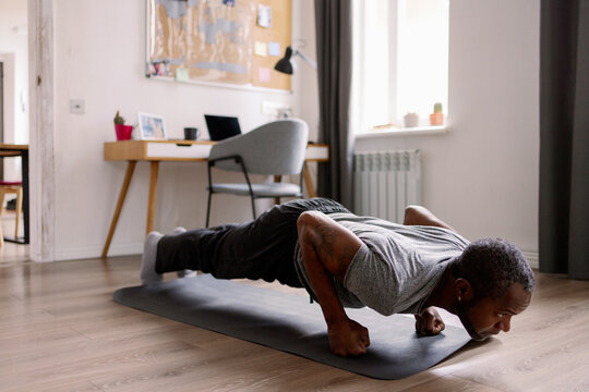 Adult black man doing push ups on fists on fitness mat in living room