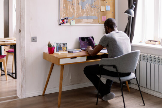 Black man watching stock market graph on laptop in chair at desk