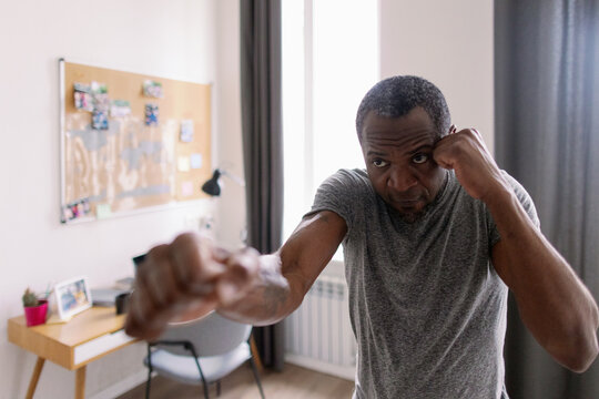 Adult black man training fighting boxing in blurred room at home