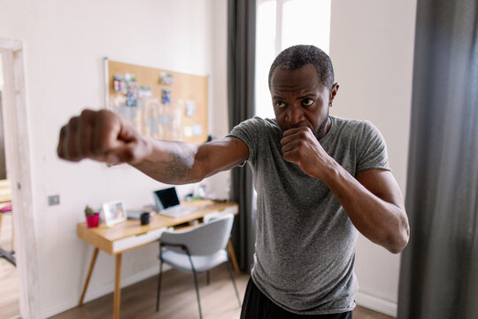 Adult black bearded man training fighting boxing in living room