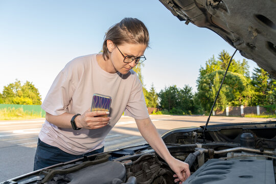 Woman Inspecting Car Engine While Holding Smartphone