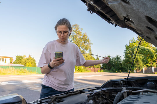 Woman checking phone while inspecting car engine.