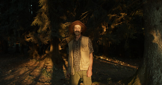 Man with a hat stands in a forest during sunset