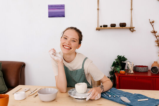 Happy lady potter crafting ceramic dishware in workshop