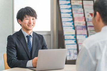 ショールーム・商談スペースで接客する若いアジア人ビジネスマンと女性客 © buritora