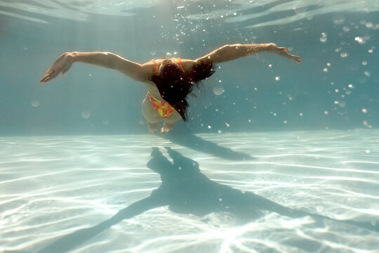 Woman is posing underwater in sunny swimming pool