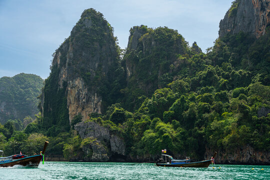 Long-tail boat speeding through turquoise water past jungle cliffs near Railay Beach