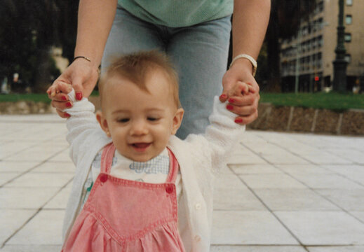 A baby girl is learning how to walk with a little help of her mother