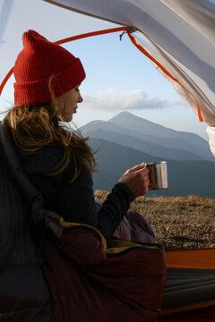 Girl in sleeping bag in tent  with hot tea in cup.