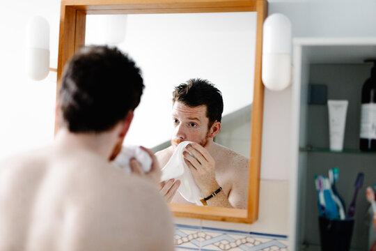 Man with red hair softly pats his face dry with a hand towel