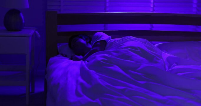 Man turning off night lamp and going to sleep in bed. Camera moving down