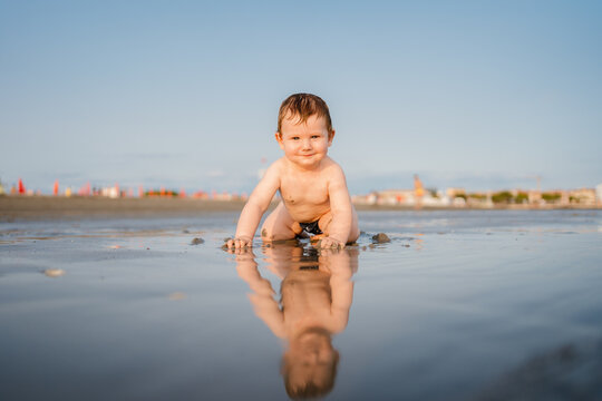 An infant crawling on the shoreline at the beach