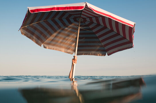 Hand holding beach umbrella in the sea