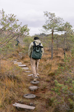Hiker with green backpack on wooden forest path.