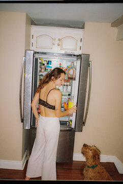 Dog sitting beside the woman when she is looking in the fridge 