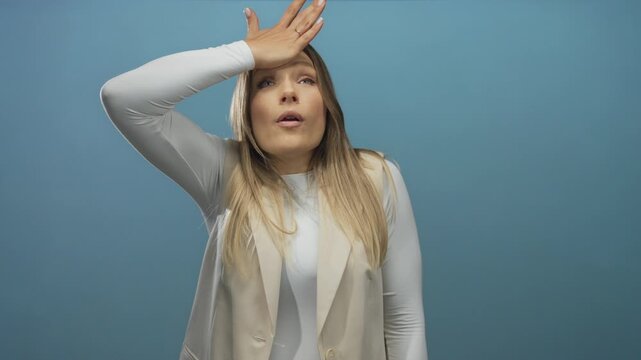 Woman holding forehead in realization against isolated blue wall expressing surprise in modern attire