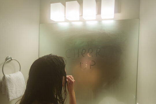 Woman after shower looking in the mirror with written "cheer up" on it