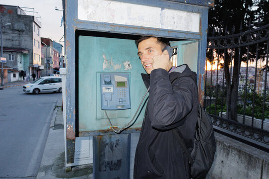 A young man is talking on a pay phone