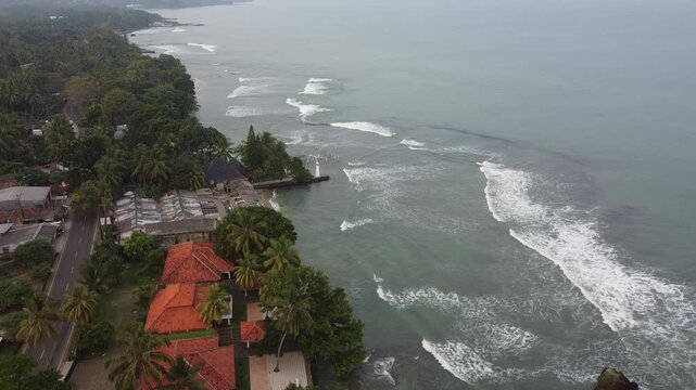 A smooth drone shot glides over Anyer Beach, Indonesia, revealing golden shoreline, gentle waves, and clear tropical waters stretching along the scenic Banten coast
