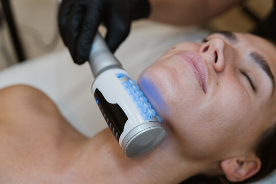Beautician performing led light therapy treatment on woman's face