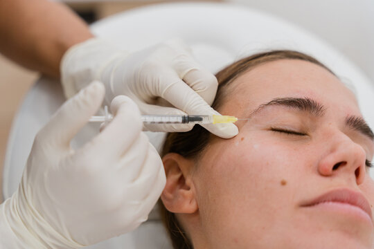 Beautician injecting botulinum toxin near eye of woman