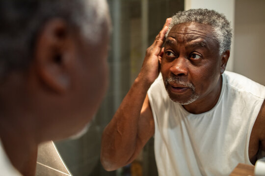 Senior man checking his face in bathroom mirror