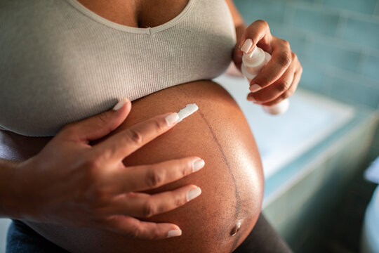 Pregnant woman applying belly lotion at home