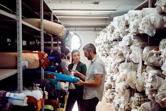 Two coworkers inspecting fabric rolls in a textile warehouse