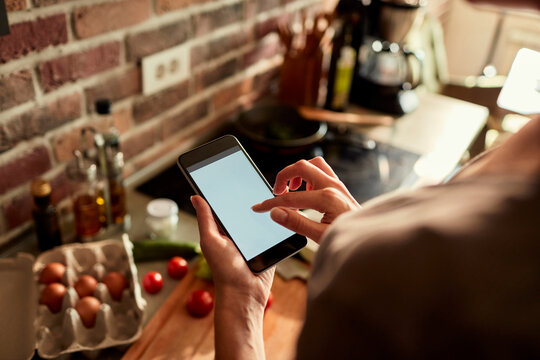 Person using smartphone with blank screen while cooking in home kitchen