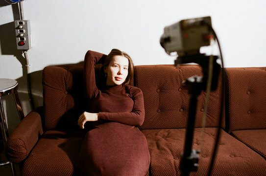 Woman relaxes on brown couch while being filmed